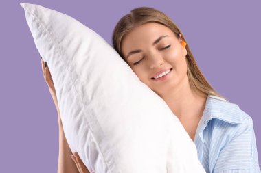 Kulak tıkacı ve eflatun kaplama yastıklı genç bir kadın.