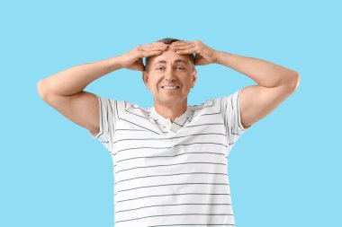 Mutlu olgun bir adam mavi arka planda yüz geliştirme egzersizi yapıyor.