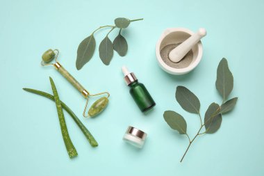 Farklı doğal kozmetik ürünlere sahip kompozisyon, yüz masajı silindiri, okaliptüs ve turkuaz arka planda aloe vera yaprakları