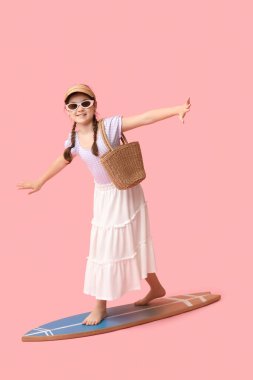 Sörf tahtasında pembe arka planda hasır çantalı tatlı bir kız.