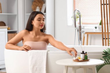 Güzel genç bir kadın küvette oturuyor ve evde banyo bombası taşıyor.