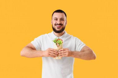 Sarı arka planda lezzetli sandviçli genç adam.