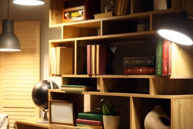 Akşamları şık bir odada farklı kitap ve dekor içeren kitaplık, yakın plan.