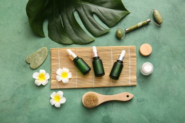 Yeşil grunge arka planında bambu tepsisi, çiçek, kavanoz ve kozmetik ürünleri içeren spa kompozisyonu