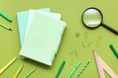 Yeşil arka planda not defterleri ve büyüteç. Üst görünüm
