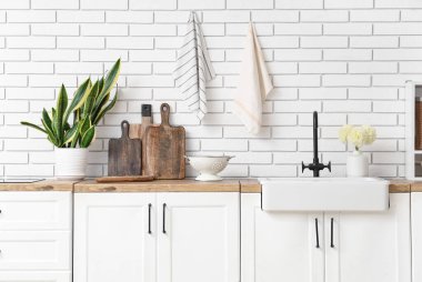White kitchen counters with sink, utensils and houseplant near white brick wall