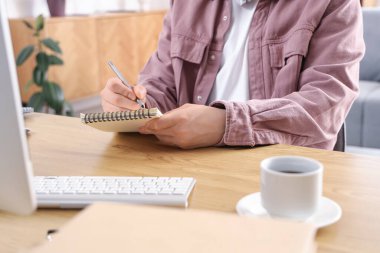 Erkek öğrenci evde çalışırken not alıyor, yakın çekim yapıyor.