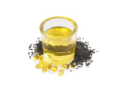 Beyaz zemin üzerinde susam tohumları ve bir bardak yağ