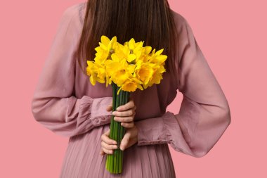 Pembe arka planda güzel narsisli çiçeklerle dolu buketi olan güzel genç bir kadın.