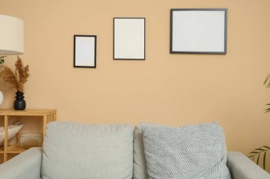 Şık bir oturma odası, rahat bir kanepe ve bej duvarda boş resim çerçeveleri.