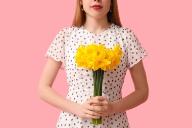 Pembe arka planda bir buket güzel nergis çiçeğiyle genç bir kadın.