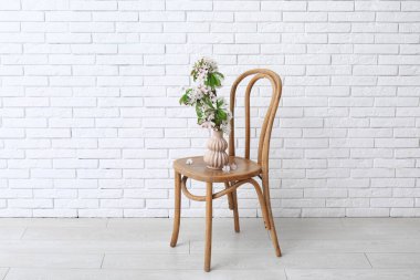 Odadaki beyaz tuğla duvarın yanındaki sandalyede çiçek açan dalları olan vazo.