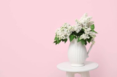 Oturma odasındaki pembe duvarın yanındaki sehpanın üzerinde leylak dalları olan vazo.