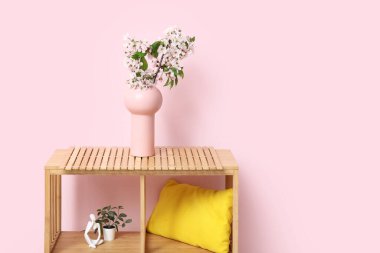 Odadaki pembe duvarın yanındaki rafta çiçek açan dalları olan vazo.