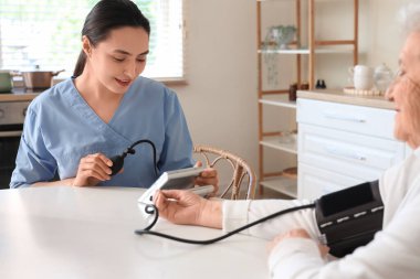 Mutfaktaki masada yaşlı kadının kan basıncını ölçen fizyoterapist.