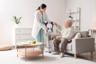 Evde koltuk değnekleriyle kıdemli kadın ve fizyoterapist.