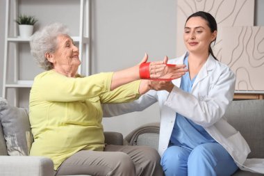 Evde esneme bandı ve fizyoterapisti olan yaşlı bir kadın var.