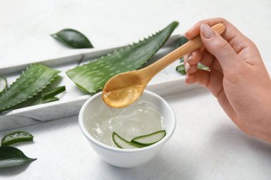 Beyaz arka planda kaşık ve bir kase aloe vera jeli olan kadın eli.