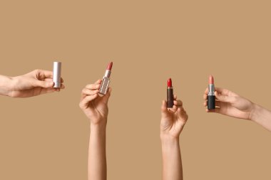 Kahverengi arka planda bir sürü ruju olan kadın elleri.