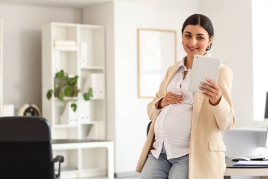 Ofisinde tablet bilgisayarı olan hamile bir iş kadını.