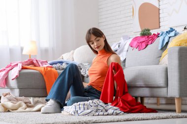 Dağınık giysileri olan güzel, genç, mutlu bir kadın dağınık bir odada yerde oturuyor.