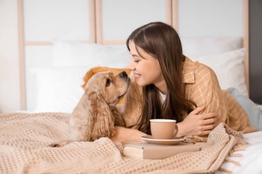 Güzel, genç, mutlu bir kadın ve evde yatağında bir fincan yeşil çayla Cocker Spaniel köpeği.