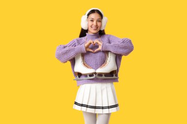 Sarı arka planda kalp hareketi gösteren buz patenli güzel bir Asyalı kadın.