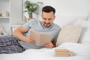 Yatak odasında kitap okuyan yakışıklı bir adam.