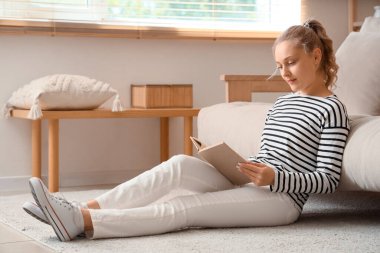 Evdeki halıda kitap okuyan güzel sarışın kadın.
