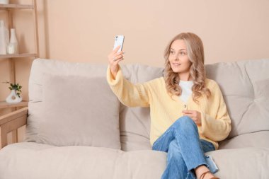 Cep telefonlu güzel sarışın kadın evdeki kanepede selfie çekiyor.