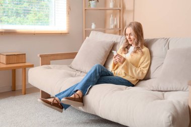 Evdeki koltukta cep telefonu kullanan güzel sarışın kadın.