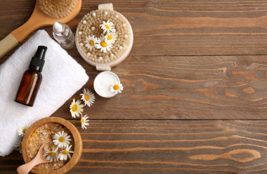 Papatya çiçekleri, masaj vücut fırçaları ve ahşap arka planda bulunan kozmetik ürünler, yakın plan.