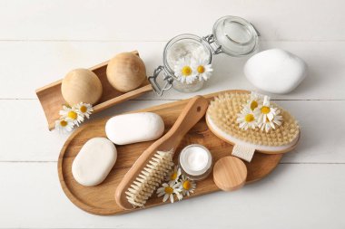 Tepsiyle spa kompozisyonu, papatya çiçekleri ve beyaz ahşap arka planda masaj vücut fırçası, yakın plan.