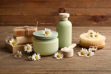 Ahşap zemin üzerinde papatya çiçekleri, şişe ve kozmetik ürünler kavanozu olan kompozisyon, yakın plan