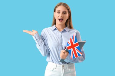 İngiliz bayrağı ve mavi arka planda bir şeyler gösteren not defterleriyle şaşırmış kadın İngilizce öğretmeni.