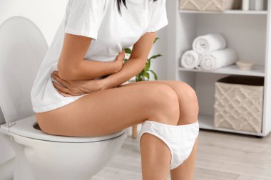 Tuvaletteki klozette adet sancısı çeken genç bir kadın.