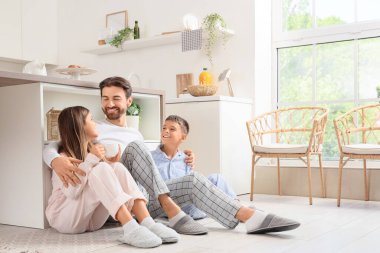 Mutlu baba mutfakta yerde çocuklarına sarılıyor.