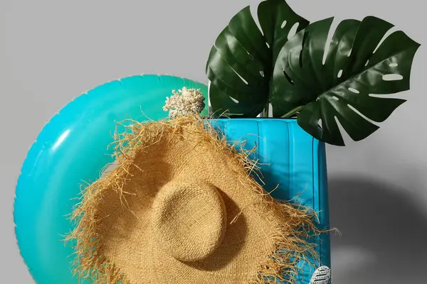 Gri arkaplanda plaj aksesuarları olan mavi bavul.