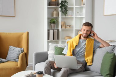 Bilgisayarlı genç sakallı adam evdeki koltukta cep telefonuyla konuşuyor.