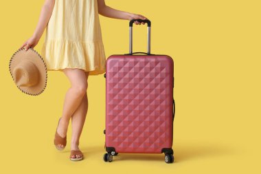 Sarı arka planda bavulu ve şapkası olan genç bir kadın.