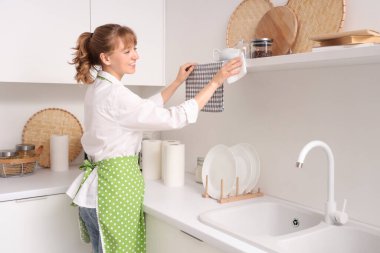 Genç bir kadın mutfakta kağıt havluyla rafları siliyor.