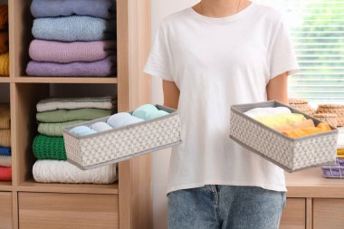 Evde katlanmış temiz giysileri olan organizatörleri tutan genç bir kadın var.