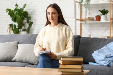 Evdeki kanepede kitap yığınıyla ders çalışan güzel, mutlu kız öğrenci.