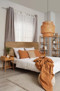 Yatak odasının içi. Yatak örtüsü buruşmuş. Yatak odası ve pencerenin yanındaki komodinin üstünde.