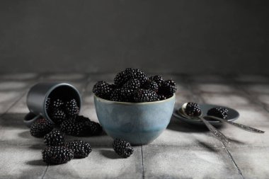 Gri fayansların üzerinde olgun böğürtlenlerle dolu bir kase ve fincan.