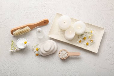 Tepsi, yanan mumlar, papatya çiçekleri ve gri grunge arka planda bir şişe kozmetik ürünü, yakın plan.