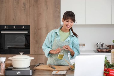 Yağ ve dizüstü bilgisayarlı genç bir kadın mutfakta sebze salatası yapıyor.