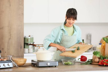 Genç bir kadın mutfakta kesilen salatalıkları kaseye koyuyor.