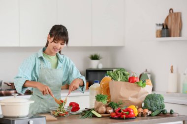 Mutfaktaki masada sebze salatası yapan genç kadın.