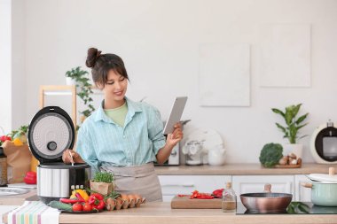 Tablet bilgisayarı olan genç bir kadın mutfakta çoklu fırın kullanıyor.
